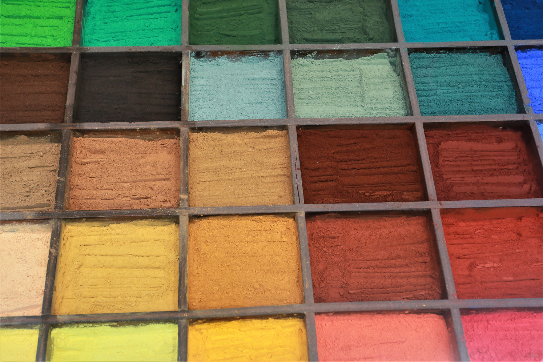 A grid of wooden boxes filled with different colour pigments.