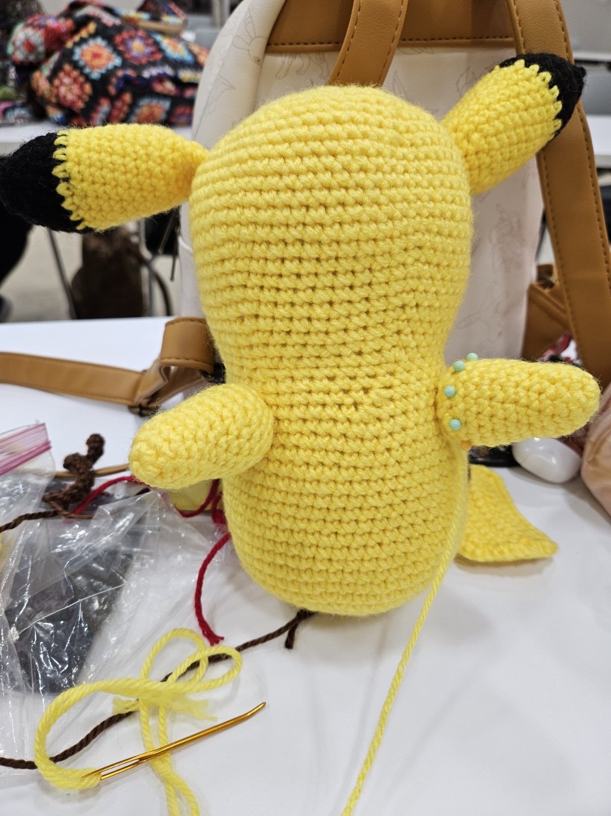 Pikachu amigurumi with his ears and one arm sewed on. The other arm is pinned but not yet sewn. The rest of his pieces have not been sewed on yet.