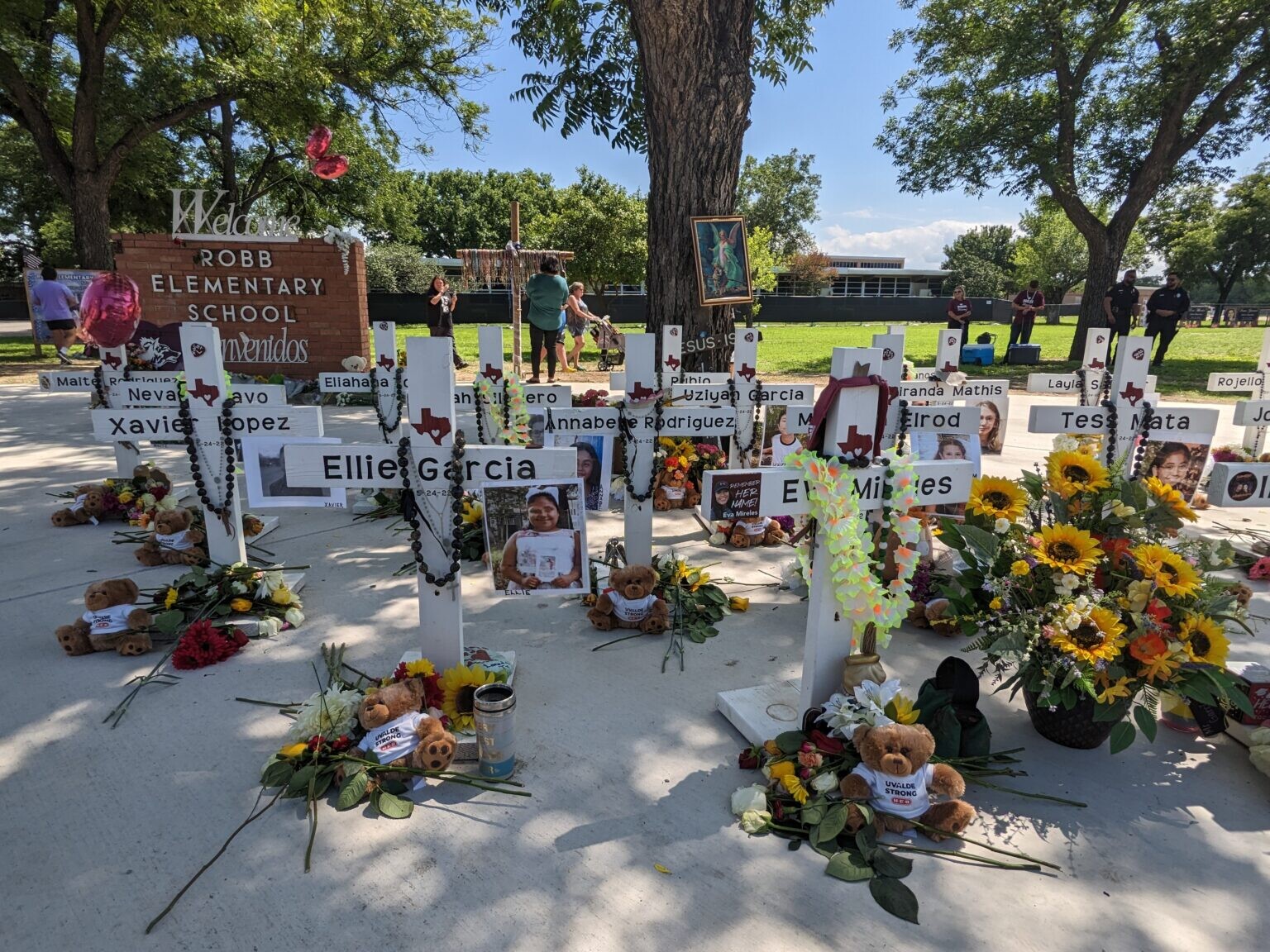 A collection of small wooden crosses, decorated with flowers and personal items, stand in memorial outside Robb Elementary School in Uvalde, Texas. 